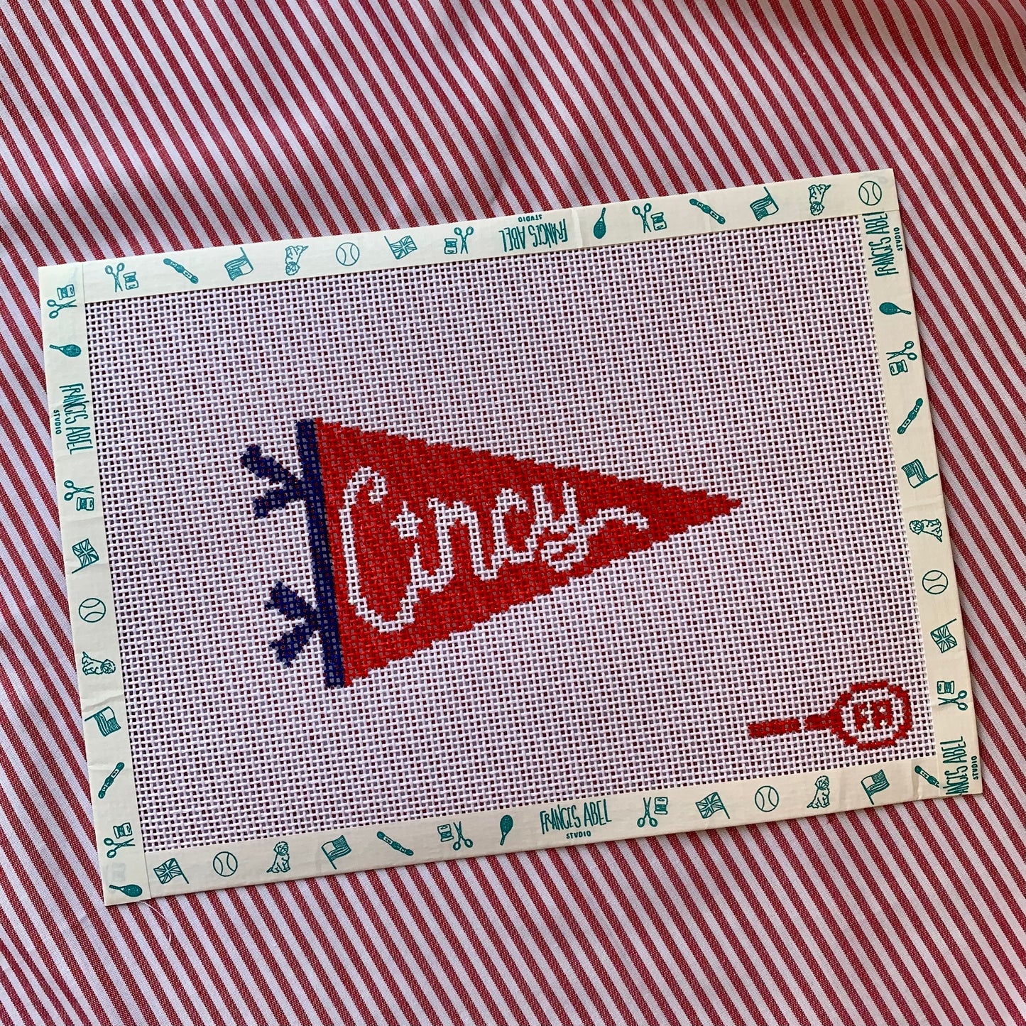 Red triangular pennant needlepoint canvas—bold white “CINCY” block lettering on a cardinal-red background with a black hoist edge, 5½ × 3″ on 14-hpi canvas for DIY décor project