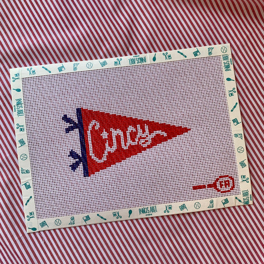 Red triangular pennant needlepoint canvas—bold white “CINCY” block lettering on a cardinal-red background with a black hoist edge, 5½ × 3″ on 14-hpi canvas for DIY décor project