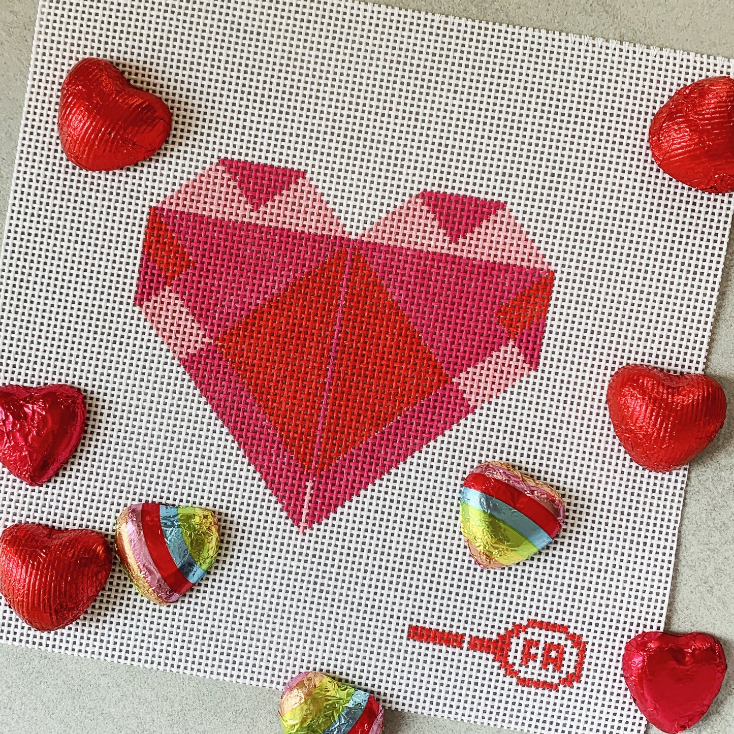 Flat-lay of Origami Heart needlepoint chart—red and pink triangulated heart on 14-mesh canvas with chocolate hearts