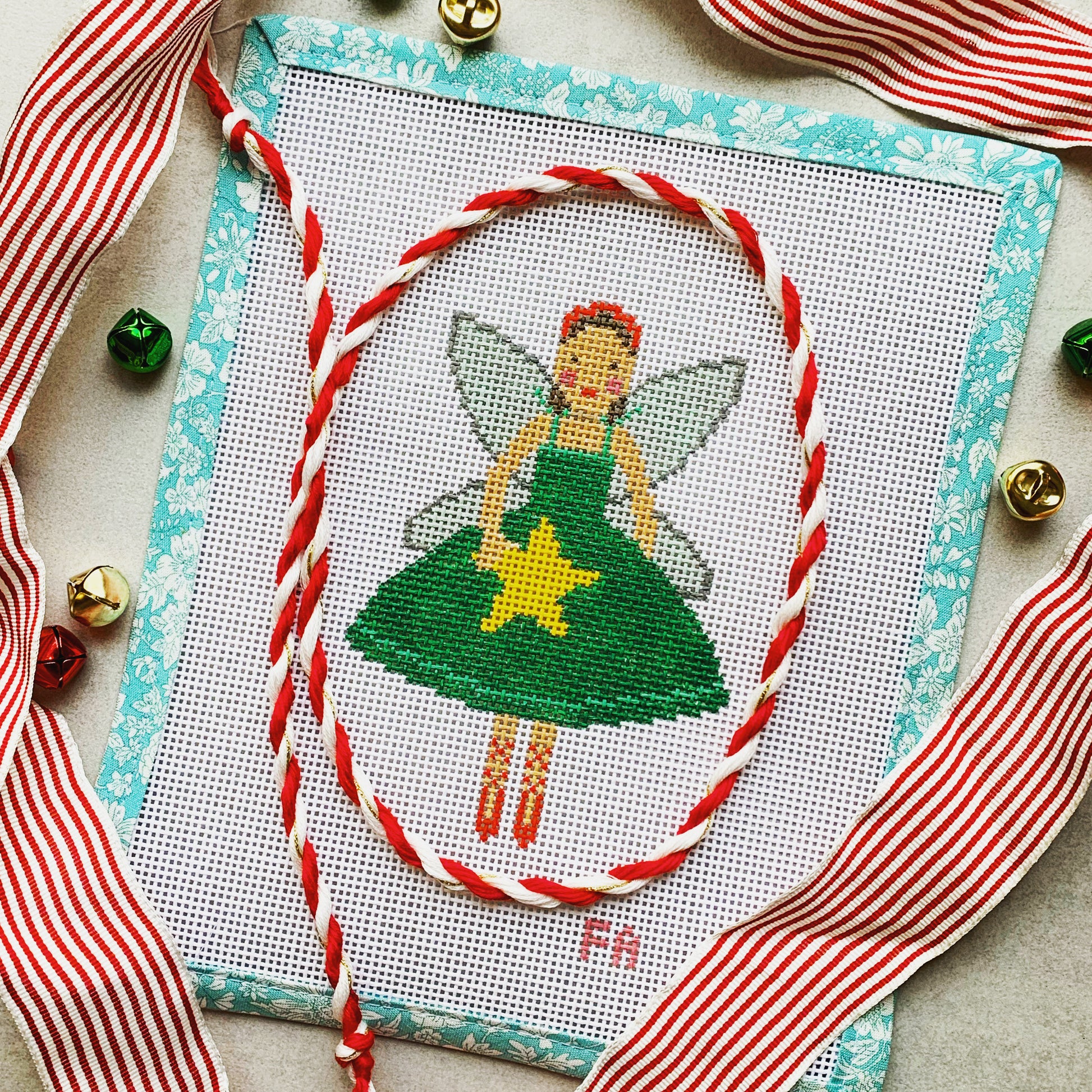  Christmas fairy needlepoint canvas featuring a ballerina-style fairy in a green dress holding a yellow star, with silver wings and a red headband, trimmed in aqua floral tape and surrounded by striped ribbon and jingle bells.