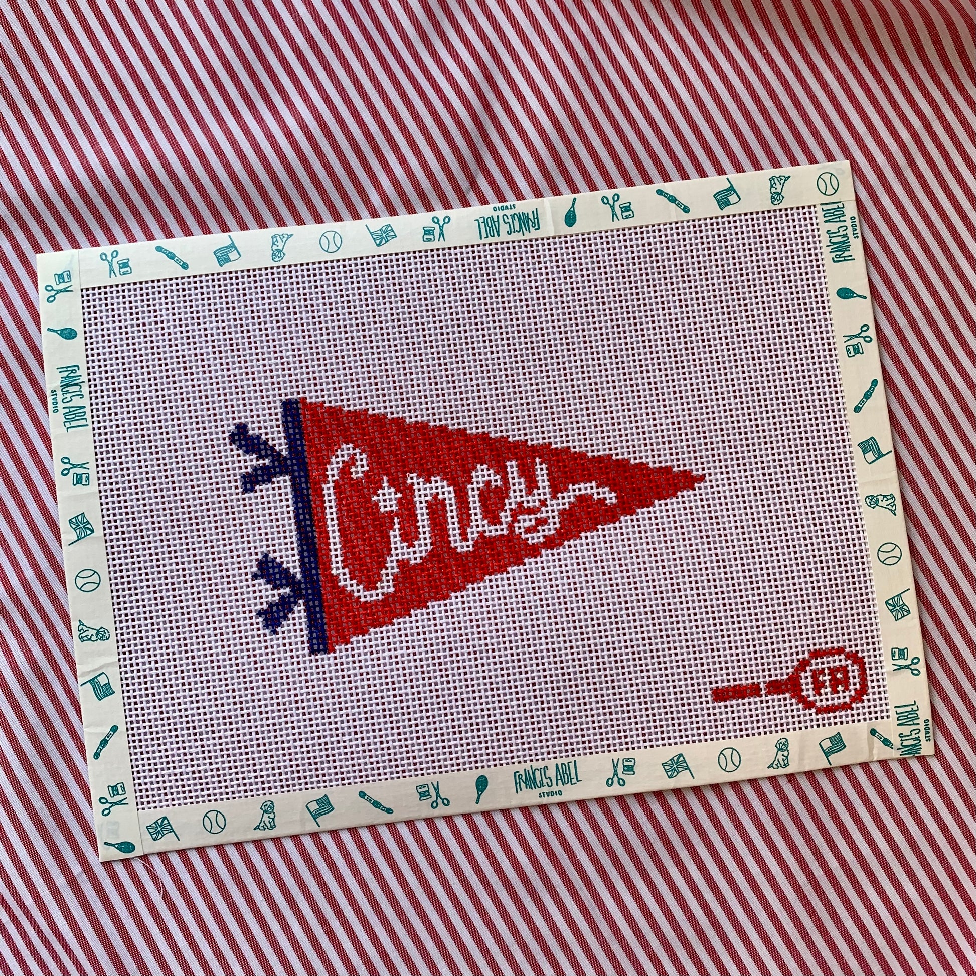 Red triangular pennant needlepoint canvas—bold white “CINCY” block lettering on a cardinal-red background with a black hoist edge, 5½ × 3″ on 14-hpi canvas for DIY décor project 

