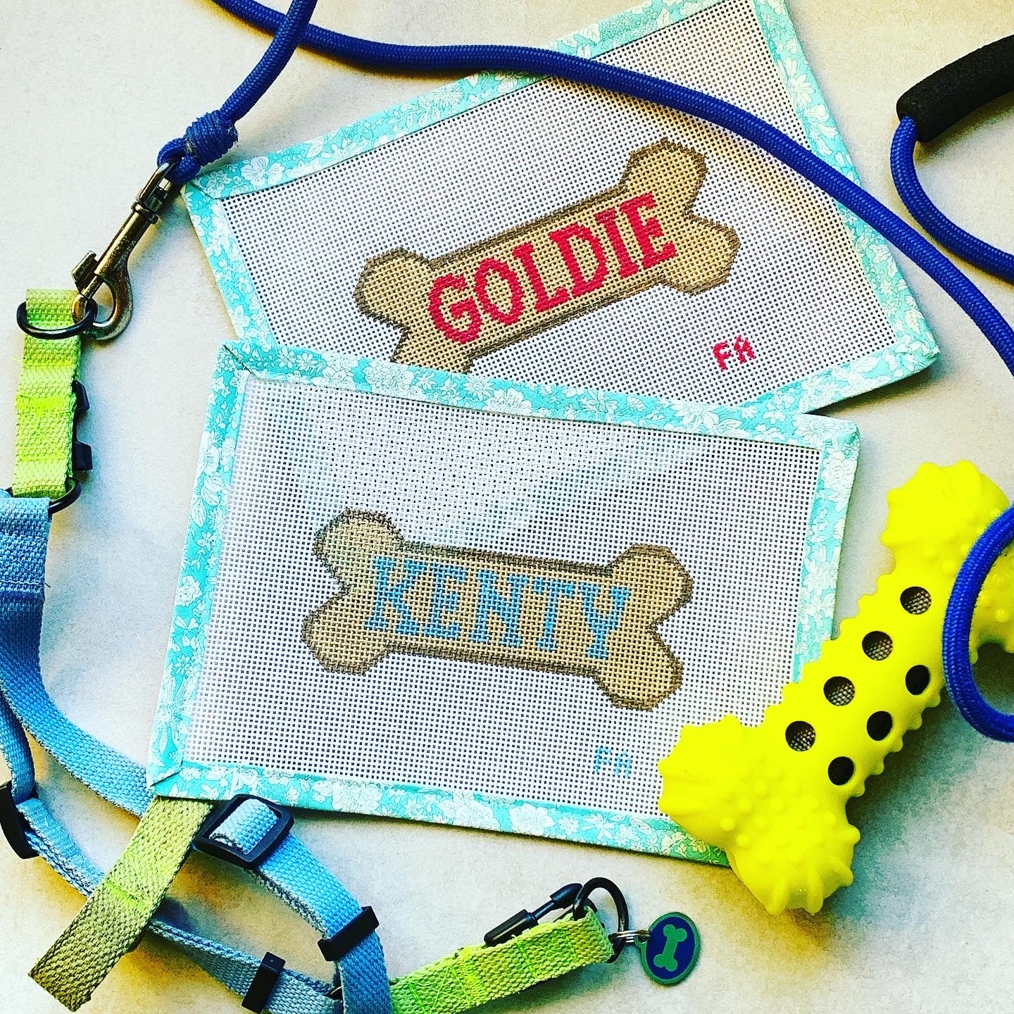 Custom dog bone needlepoint canvas with a yellow bone outlined in red, featuring space for a pet name, hand-painted on white 13 mesh with aqua floral trim.
