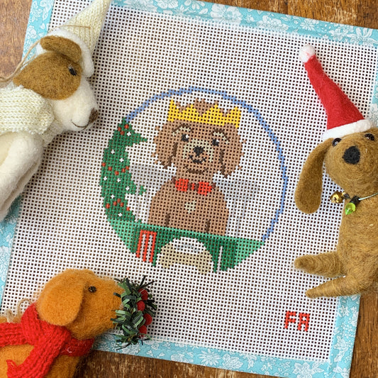 Flat-lay of a 4″ round 14 hpi needlepoint canvas brown dog with yellow crown at Christmas table with Christmas tree