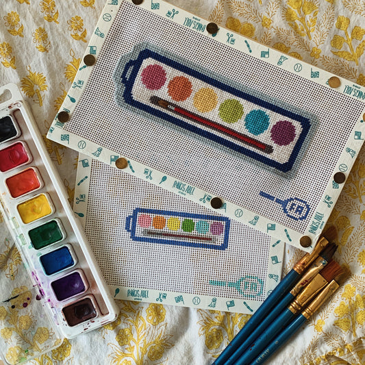 Watercolor palette needlepoint canvas kits—large and small palettes printed on natural 13-mesh, each with six rainbow-colored paint well motifs 
