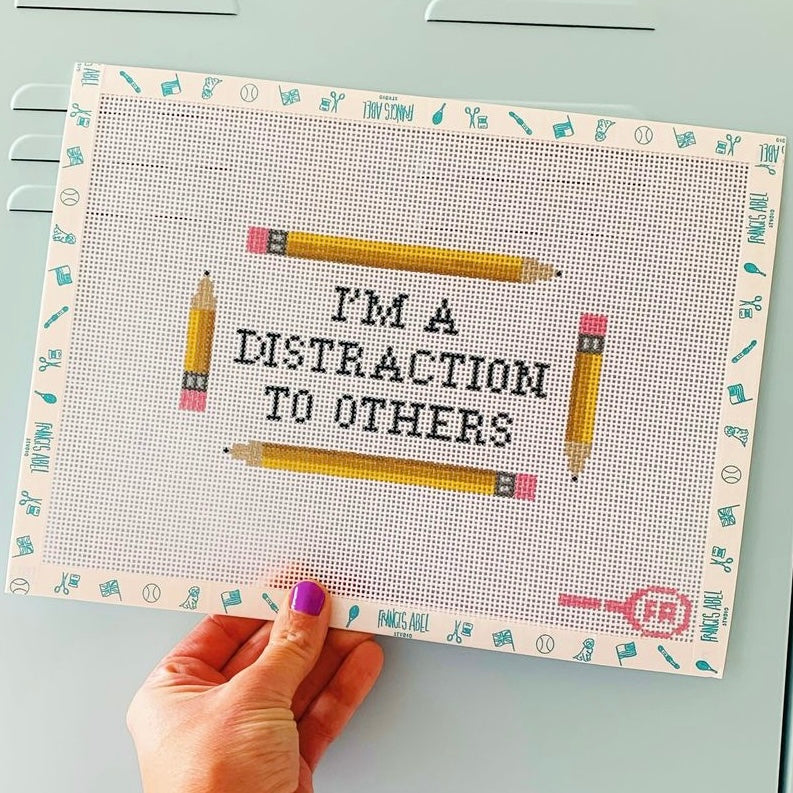 “I’m a distraction to others” printed in black block letters on natural 13-mesh canvas, 6½ × 3¾″ DIY needlepoint phrase project