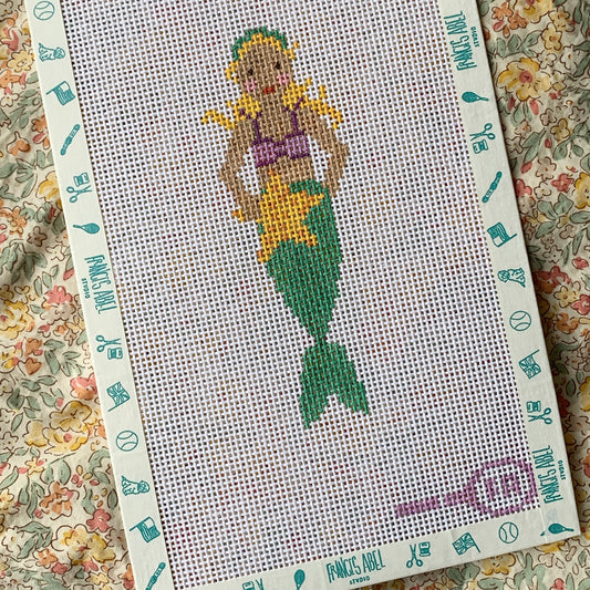 Nora’s Mermaid needlepoint canvas kit—blonde mermaid with purple seashell top, green tail, and yellow starfish on natural 13-mesh canvas, 2 × 5½″ DIY project
