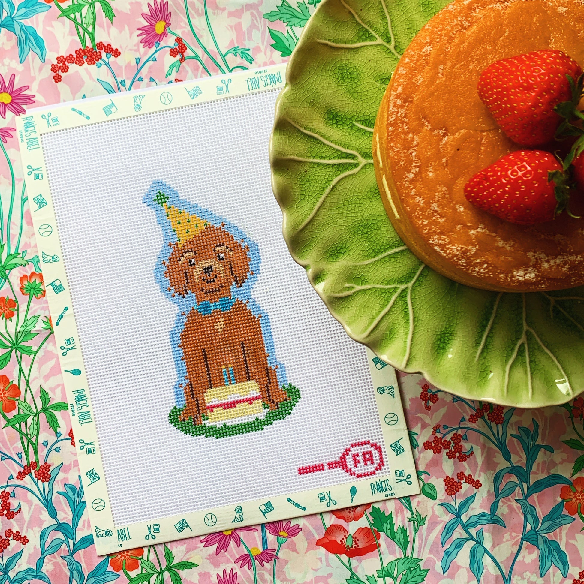 Puppy’s Birthday Cake needlepoint canvas kit—brown dog wearing a yellow party hat sitting behind a layered Victoria sponge cake on natural 14-hpi mesh, 2 7/8 × 5 3/4″ DIY project
