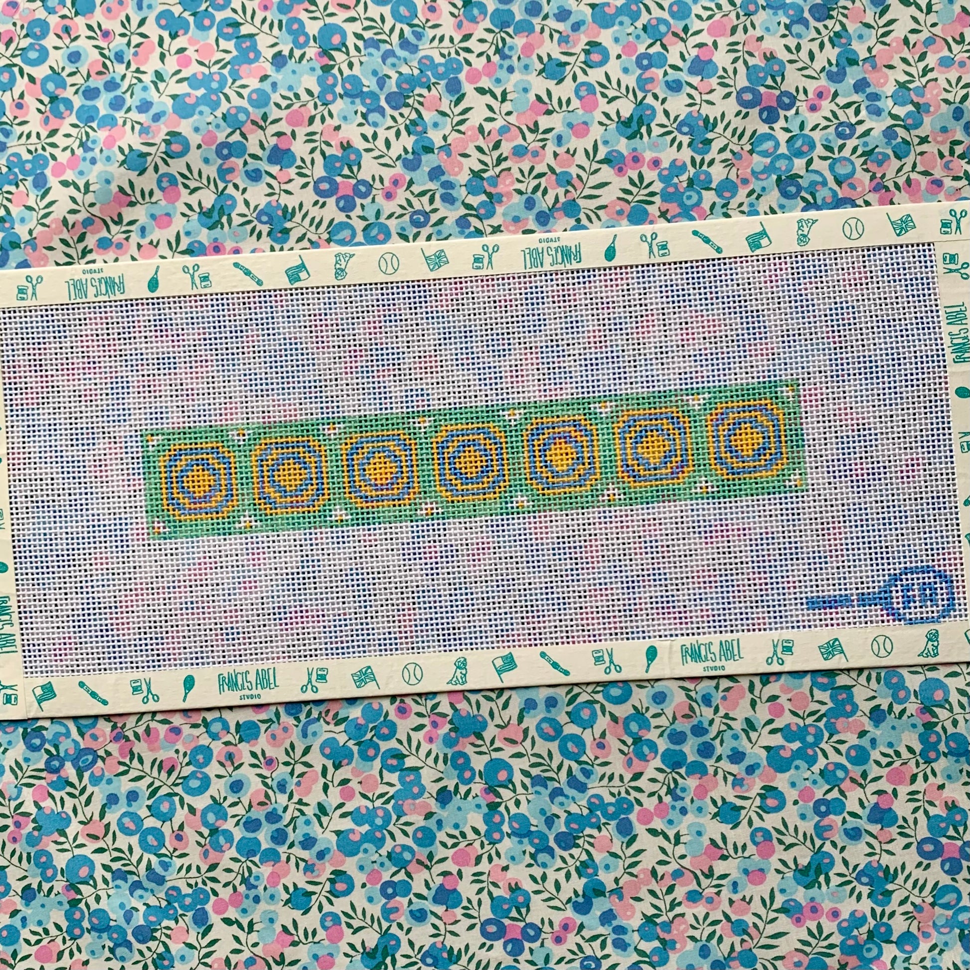 Union Station green key-fob needlepoint canvas—repeating yellow and teal circle motifs on 14-mesh with printed chart border, styled on floral background 